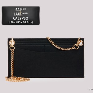 May include: A black felt handbag organizer insert featuring a gold-tone metal chain strap attached to two side rings. The insert includes multiple interior pockets and is labeled with the text SAI*** LAUR*** CALYPSO and dimensions L30 x H15 x D3.5 cm.