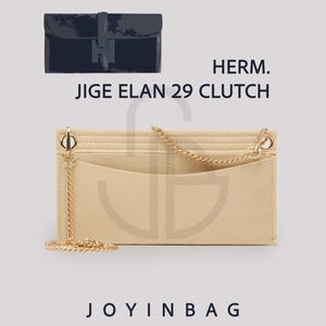 Op de afbeelding: Een beige vilten tasorganizer met een rechthoekige vorm en meerdere binnenvakken, een goudkleurige metalen ketting bevestigd aan de bovenhoeken, en de tekst HERM. JIGE ELAN 29 CLUTCH en JOYINBAG afgedrukt op de afbeelding.