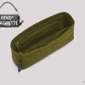Op de afbeelding: Een olijfgroene vilten handtasorganizer met meerdere binnenvakken en een goudkleurige metalen rits. Het inzetstuk is voorzien van een klein zwart stoffen label met een logo en wordt getoond naast een afbeelding van een FEND* BAGUETTE handtas.
