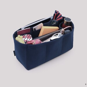May include: A navy blue felt bag organizer with multiple compartments and pockets. The organizer is filled with various items, including a phone, a tablet, a wallet, a water bottle, and other accessories.