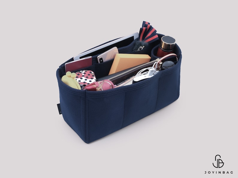 May include: A navy blue felt bag organizer with multiple compartments and pockets. The organizer is filled with various items, including a phone, a tablet, a wallet, a water bottle, and other accessories.