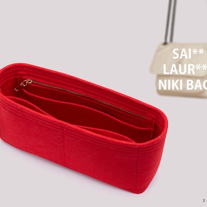 May include: A red felt handbag organizer insert with multiple interior compartments and a zippered pocket. A small black tag with the text JOYINBAG is attached to the side. In the background, a beige shoulder bag is visible with the text SAI** LAUR*** NIKI BAGS.