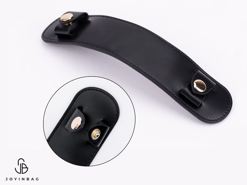 Puede incluir: Asa de cuero negro con detalles en metal dorado. El asa es curva y tiene dos peque&ntilde;os bucles en cada extremo.