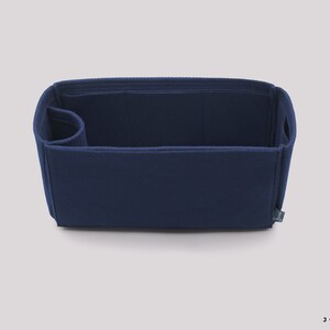 May include: A navy blue felt bag organizer with multiple compartments and a small pocket on the side. The organizer is designed to fit inside a larger bag and help keep it organized.