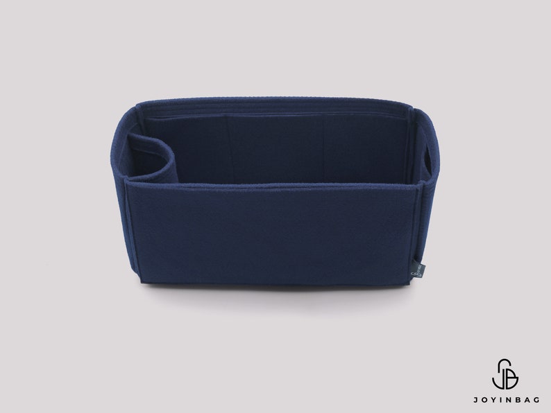 May include: A navy blue felt bag organizer with multiple compartments and a small pocket on the side. The organizer is designed to fit inside a larger bag and help keep it organized.
