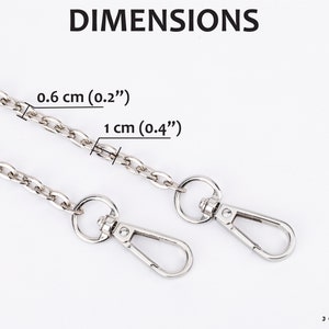 Może przedstawiać: Srebrny łańcuch z dwoma srebrnymi zapięciami. Łańcuch ma szerokość 0,6 cm i 0,4 cm. Tekst "DIMENSIONS" znajduje się w g&oacute;rnej części obrazu. Tekst "0,6 cm (0,2")" i "1 cm (0,4")" znajduje się pod łańcuchem. Tekst "JOYINBAG" znajduje się w dolnej części obrazu.