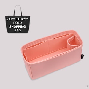May include: A light pink felt handbag organizer insert featuring multiple interior compartments and a cylindrical side pocket. A black shopping bag graphic with the text SAI** LAUR*** BOLD SHOPPING BAG is visible in the upper left corner.