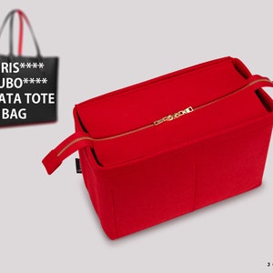 Peut inclure: Organiseur de sac en feutre rouge avec une fermeture éclair dorée. Le sac a une poche zippée sur le dessus et une poche plus petite sur le côté. Le sac est conçu pour s'adapter à l'intérieur d'un sac cabas plus grand.