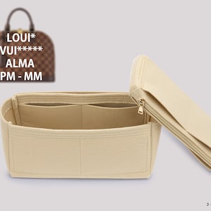 Puede incluir: Organizador de bolso de fieltro beige con múltiples compartimentos y una parte superior con cremallera. El organizador está diseñado para caber dentro de un bolso Louis Vuitton Alma PM - MM.