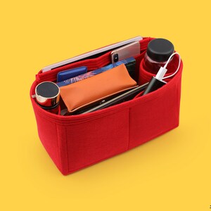 May include: Red felt bag organizer with multiple compartments. The organizer is filled with various items, including a phone, a water bottle, a wallet, and a charging cable.