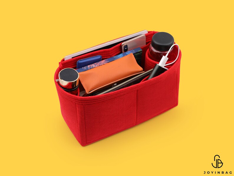 May include: Red felt bag organizer with multiple compartments. The organizer is filled with various items, including a phone, a water bottle, a wallet, and a charging cable.