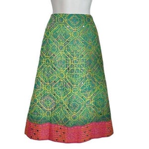 May include: A green and yellow patterned skirt with a pink and gold trim. The skirt has a geometric design with sequins.