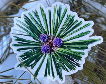May include: A close-up of a green pine cone with purple flower buds. The pine cone is on a white background.