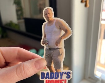 May include: A sticker featuring a man holding a can of beer with the text "Daddy's Home!" in red and blue letters.