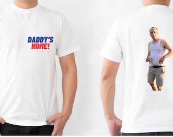 May include: White t-shirt with the text "DADDY'S HOME!" in blue and red letters on the front. The back of the shirt features a photo of a man wearing a white tank top and khaki shorts.