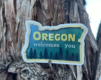 May include: A green and yellow sticker shaped like the state of Oregon with the text "Oregon welcomes you" and a row of evergreen trees along the bottom.