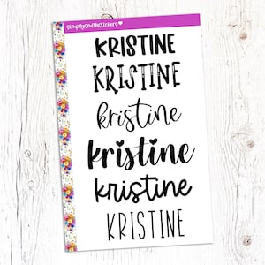 May include: A white sheet of paper with the name "Kristine" written in six different styles. The name is written in all caps, lowercase, and with a heart over the "i".