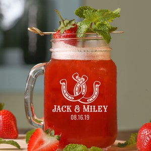 May include: A mason jar filled with a red beverage, garnished with a strawberry and mint leaves. The jar has a handle and is etched with two horseshoes, the text "Jack & Miley", and the date "08.16.19".