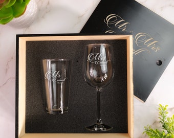 Puede incluir: Una caja de madera negra con un interior de espuma contiene dos vasos grabados. Un vaso es una copa de vino con el texto "Mrs. Caldwell" y el otro es un vaso de pinta con el texto "Mr. Caldwell".