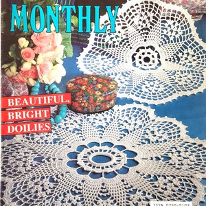 May include: Crochet Monthly magazine cover featuring two white crocheted doilies on a blue background. The magazine title is "Crochet Monthly" and the text "Beautiful, Bright Doilies" is below the doilies. The magazine issue number is 144 and the price is £1.20.