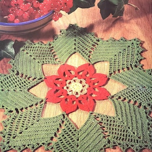 May include: A green crocheted doily with a red crocheted flower in the center. The doily has a scalloped edge and is made with a delicate stitch.