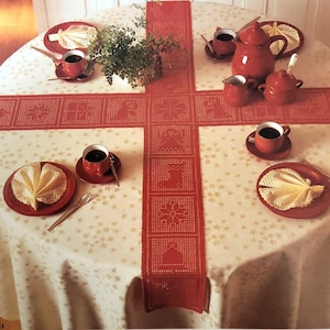 Może przedstawiać: Biały obrus w czerwone gwiazdki jest zastawiony czterema nakryciami. Każde nakrycie zawiera czerwoną podstawkę, białą filiżankę, białą serwetkę i czerwony talerz. Czerwony, szydełkowy bieżnik ze wzorem płatka śniegu i choinki biegnie wzdłuż środka stołu. Na stole stoi czerwony czajnik i dzbanek.