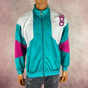 May include: A vintage Adidas track jacket in teal, white, and fuchsia. The jacket features a full zipper, a stand-up collar, and the Adidas logo on the sleeve. The jacket is displayed on a mannequin.