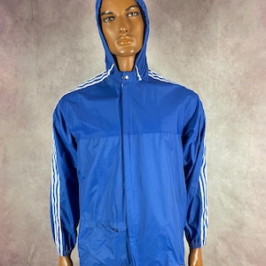 May include: A blue hooded jacket with white stripes on the sleeves and shoulders. The jacket has a zipper closure and a small pocket on the front. The jacket is displayed on a mannequin.
