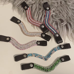 以下が含まれることがあります： 曲線状の5色のラインストーンヘアタイ。ヘアタイの色は赤、白、青、薄いピンク、薄い青、緑です。