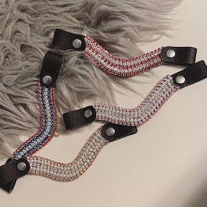 以下が含まれることがあります： 黒の革紐が付いた、赤、青、ピンクのラインストーンで飾られたヘアゴム3本。