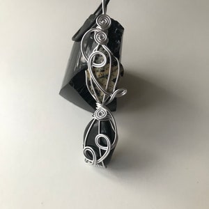 May include: A silver wire wrapped pendant featuring a black and white dalmatian jasper stone and a black obsidian stone.