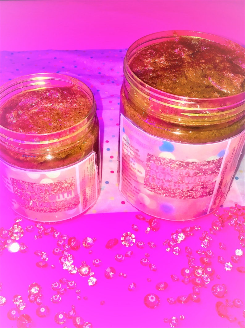 Puede incluir: Dos tarros de vidrio llenos de un exfoliante de az&uacute;car moreno. Los tarros tienen etiquetas rosas y azules con purpurina y el texto "This is all you need to get that glow". Los tarros est&aacute;n sobre una superficie rosa con gemas de pl&aacute;stico transparentes esparcidas a su alrededor.