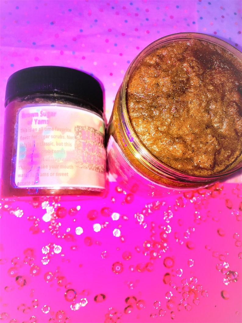 Puede incluir: Primer plano de un tarro de vidrio lleno de exfoliante de az&uacute;car moreno. El tarro tiene una etiqueta que dice "Brown Sugar Yams" y describe el producto como un sabor favorito de todos los tiempos para exfoliantes de az&uacute;car. El tarro est&aacute; sobre una superficie rosa con purpurina.