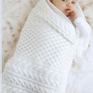 Puede incluir: Una manta de bebé de punto blanco con un patrón de trenza. La manta mide 60 x 80 cm.