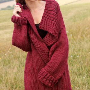 Könnte beinhalten: Ein tief roter Strickcardigan mit einem breiten, übergroßen Kragen und langen Ärmeln. Der Cardigan ist aus einem dicken Garn gefertigt und hat eine lockere Passform.