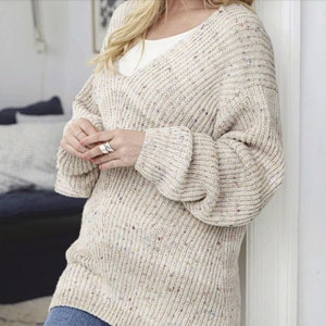 May include: A cream-coloured sweater with a v-neck and a speckled pattern. The sweater has long sleeves and a relaxed fit.