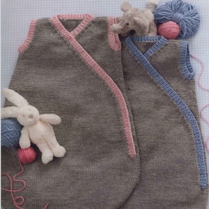 May include: Two knitted baby sleeping bags, one gray with pink trim and one gray with blue trim. The sleeping bags are laid out on a white surface with a stuffed animal and yarn.