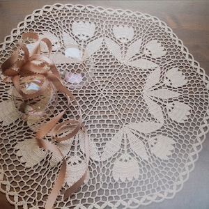 May include: A delicate crocheted doily with a floral design. The doily is made with a beige thread and features a central circle with a repeating pattern of flowers and leaves.
