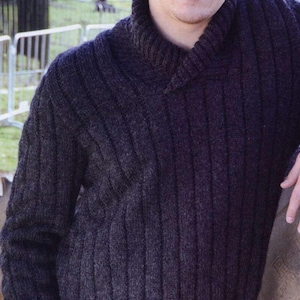 May include: A dark grey knitted jumper with a wide collar. The jumper has a ribbed texture and is made of a soft, comfortable material.