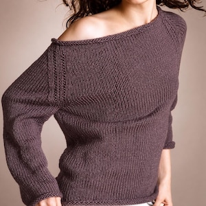 Pode incluir: Um suéter de malha roxo escuro com decote ombro a ombro. As mangas compridas têm punhos canelados e o suéter tem um padrão de malha texturizada. A peça de roupa é feita de um material macio e quente.