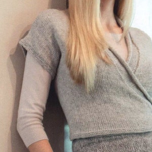 Può includere: Un top avvolgente di maglia grigio chiaro con scollo a V e chiusura avvolgente. Il top è realizzato in un tessuto morbido e leggero e ha una vestibilità rilassata.