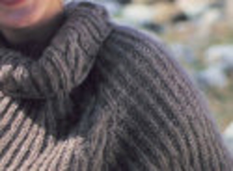 May include: Close-up of a gray knitted sweater with a cable knit pattern. The sweater has a high neck and is made of a soft, textured yarn.