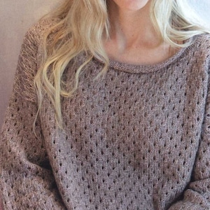 Puede incluir: Un suéter de punto marrón de corte holgado y cuello redondo. El suéter tiene un delicado patrón de calado.