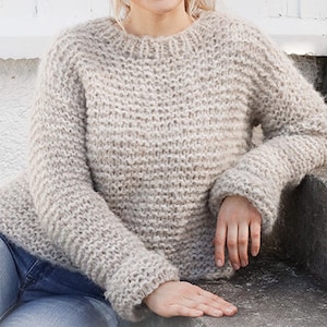 May include: A soft, light brown knitted jumper with a round neckline and long sleeves.