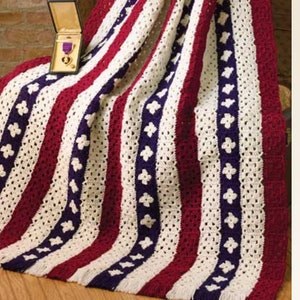 May include: A crocheted blanket with red, white, and blue stripes and a pattern of small white flowers. The blanket has a fringe border.