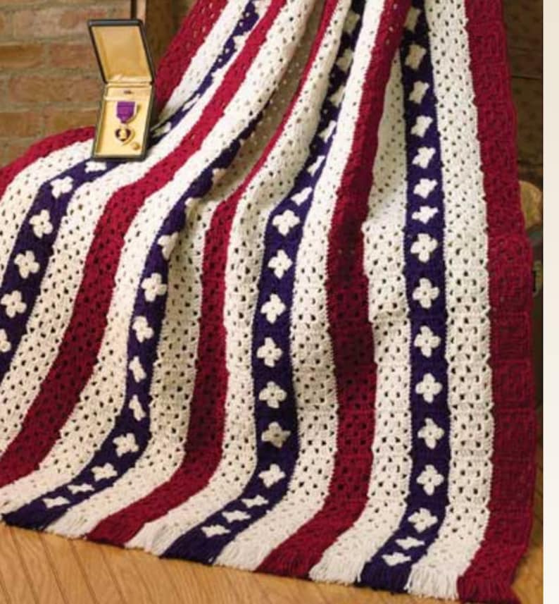 May include: A crocheted blanket with red, white, and blue stripes and a pattern of small white flowers. The blanket has a fringe border.