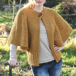 May include: A mustard yellow knitted cape with a button closure. The cape has a loose fit and is made of a soft, textured yarn.
