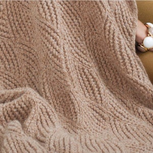 May include: A soft, brown knitted throw blanket with a textured pattern. The blanket is draped over a person's legs.
