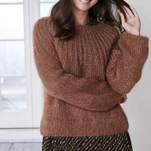 May include: A brown knitted jumper with a round neckline and long sleeves. The jumper is made of a soft, fuzzy yarn.