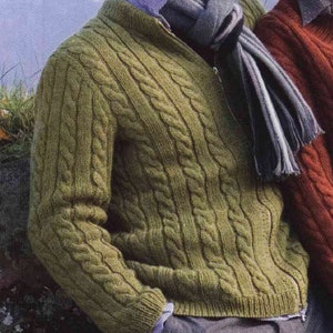 Op de afbeelding: Een groene kabelgebreide cardigan met een ritssluiting. De cardigan wordt gedragen over een lichtblauw overhemd met knopen en een gestreepte sjaal.